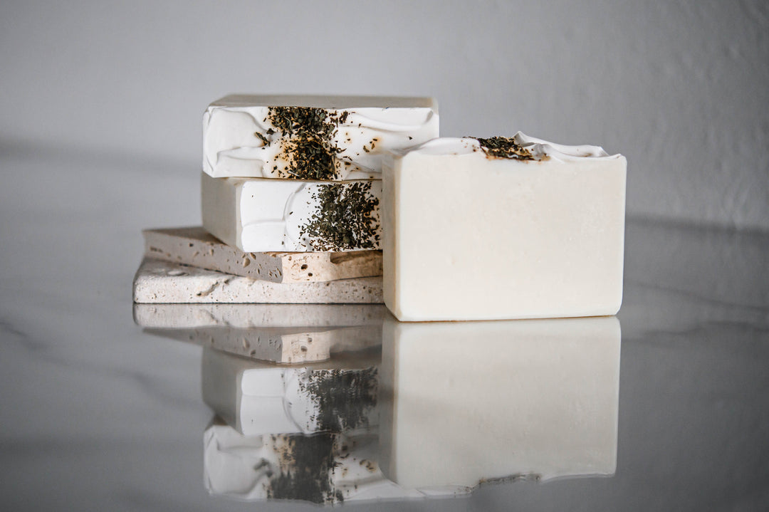 Stack of white handmade soap bars with green herb specks, rectangular with rough edges