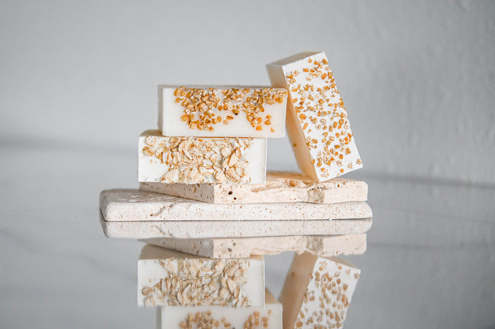 Oatmeal and honey handmade soap bars, off-white with orange speckles, stacked on gray base