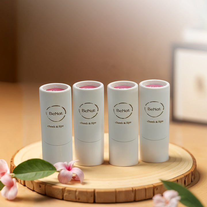 Four BeNat lip and cheek balm sticks on wooden stand with flower and leaf accents