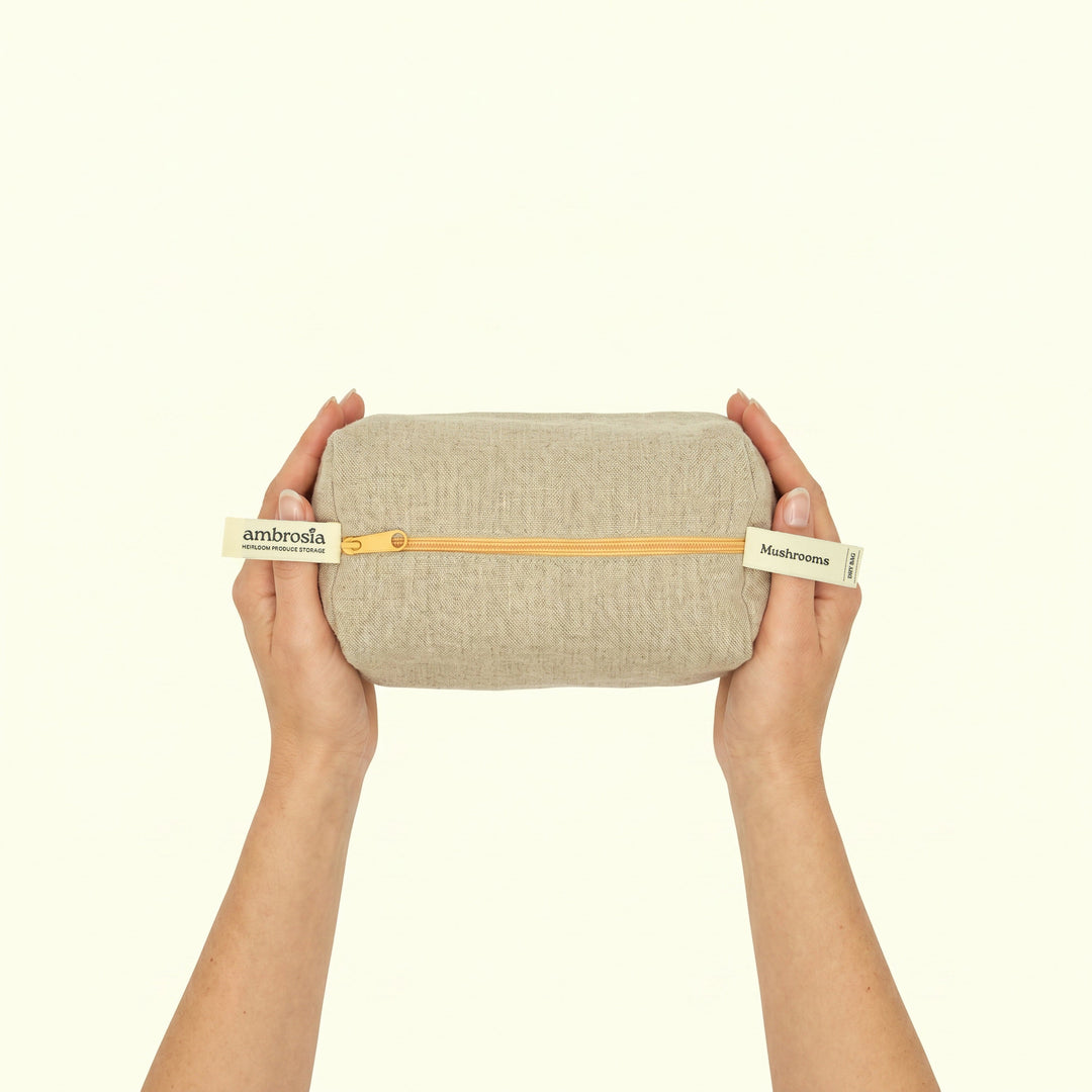 Beige linen mushroom storage bag held by hands, gold zipper along the top