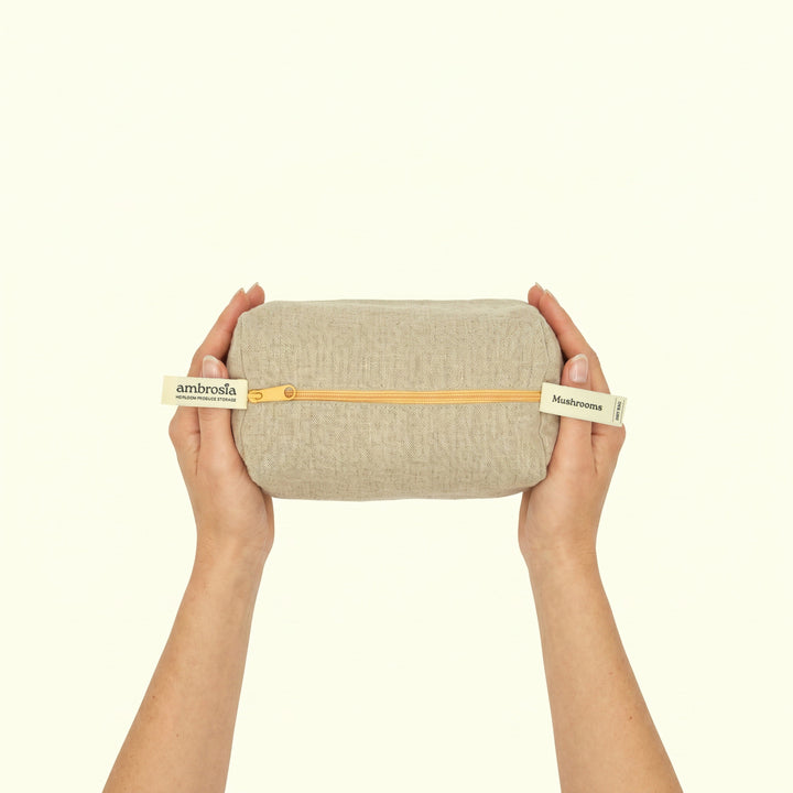 Beige linen mushroom storage bag held by hands, gold zipper along the top