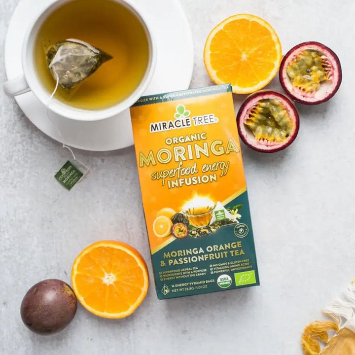 Organic moringa tea infusion pouch with cup of tea, orange slices, and passion fruit