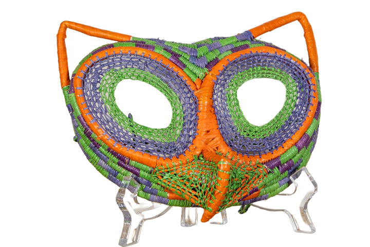 Front view of beaded yarn owl mask with orange accents, round green eye openings on blue