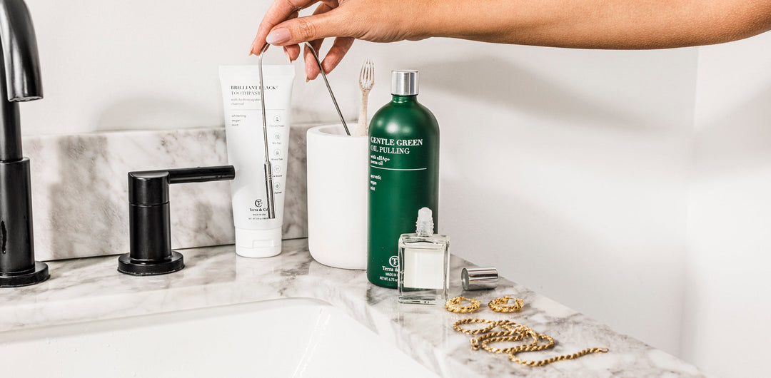 Stainless steel tongue scraper on bathroom counter beside oral care items