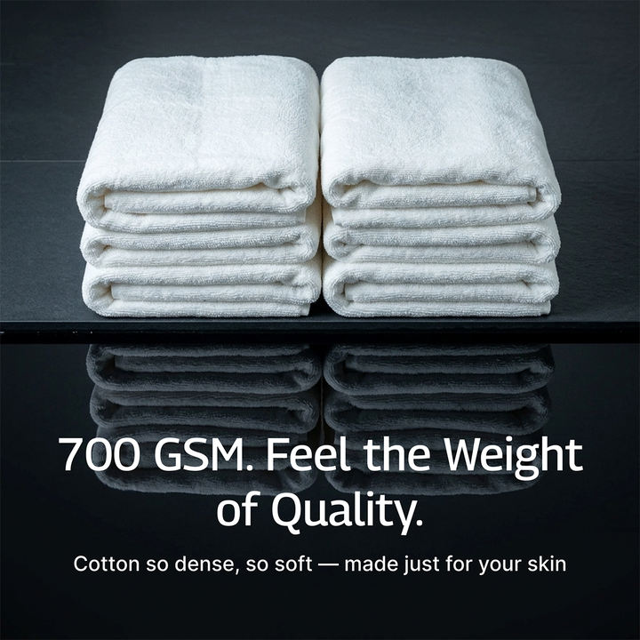 White bath towel set, four folded towels stacked on a dark surface with visible hems.