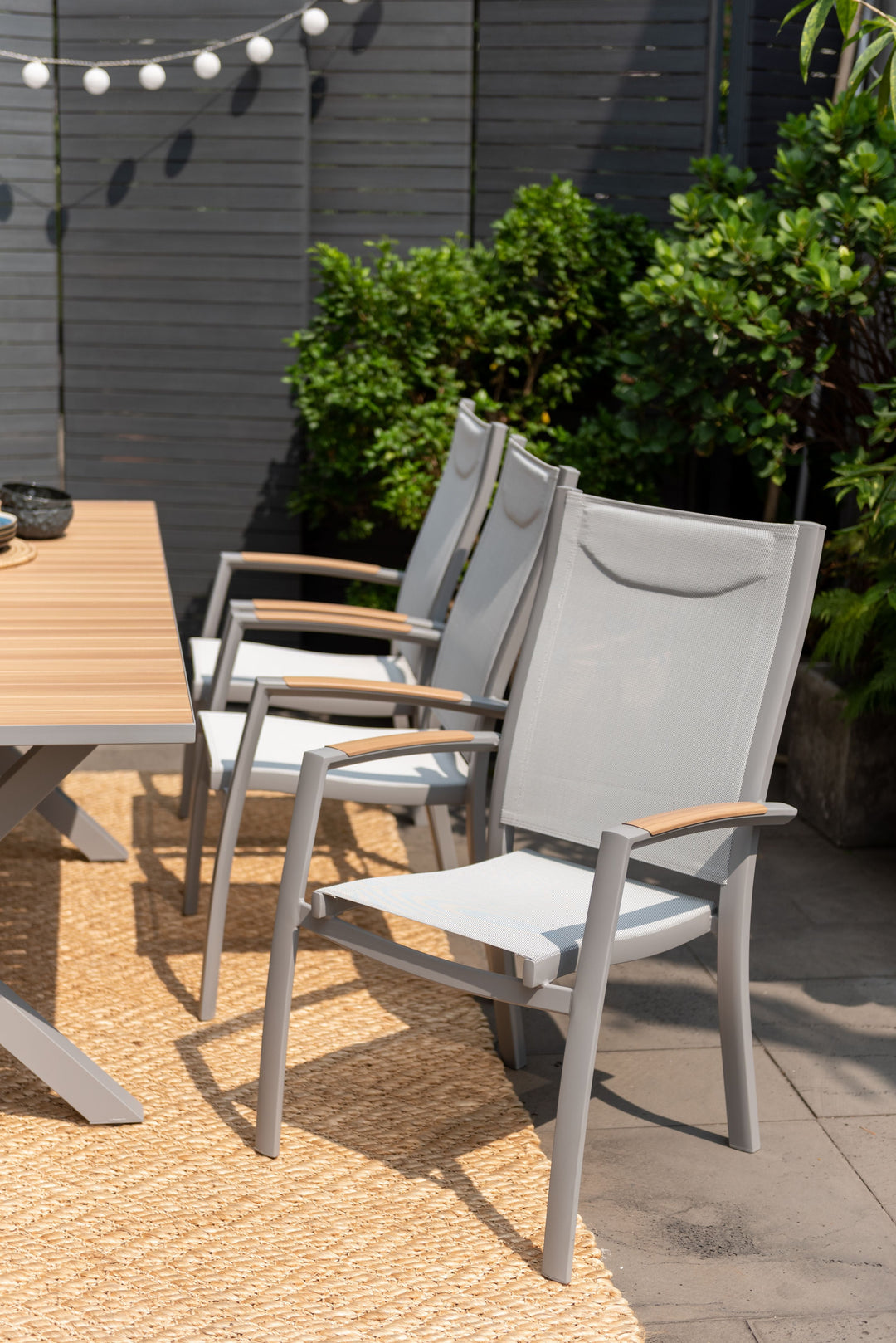 Outdoor dining chairs with gray frames and light wood armrests around a light wood table