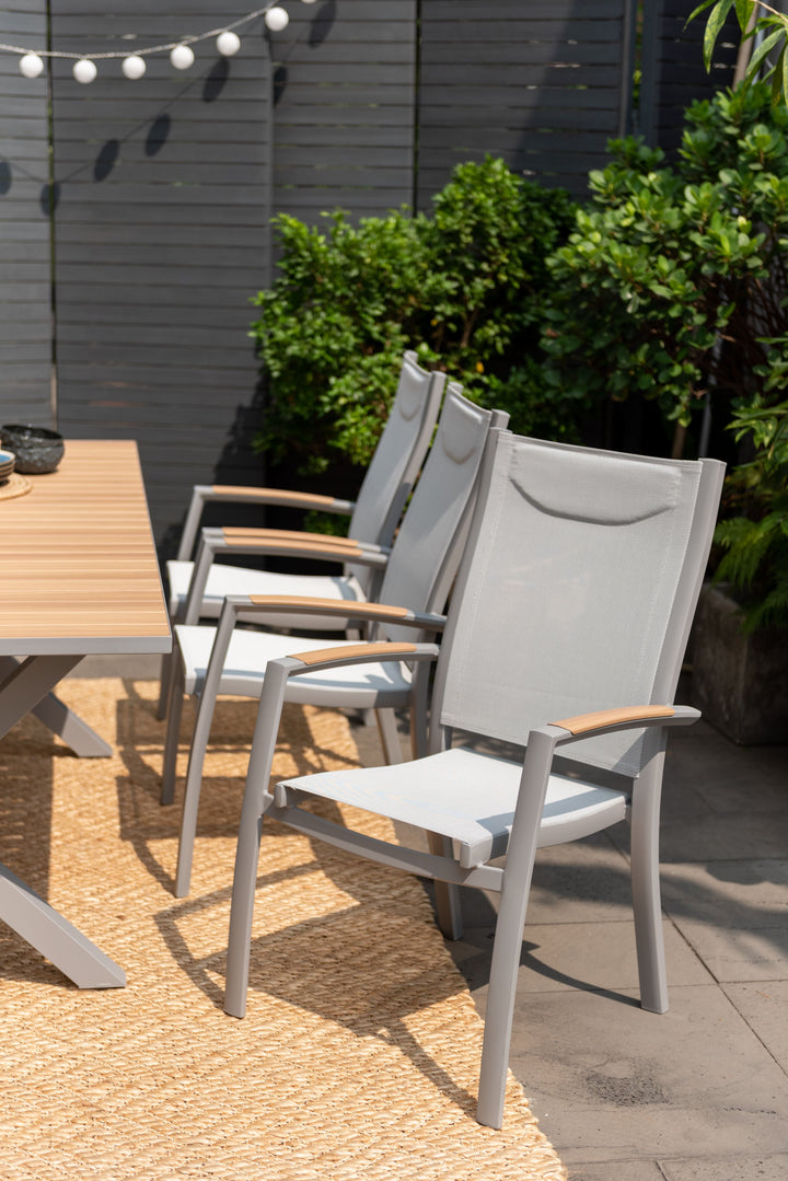 Outdoor dining chairs with gray frames and light wood armrests around a light wood table