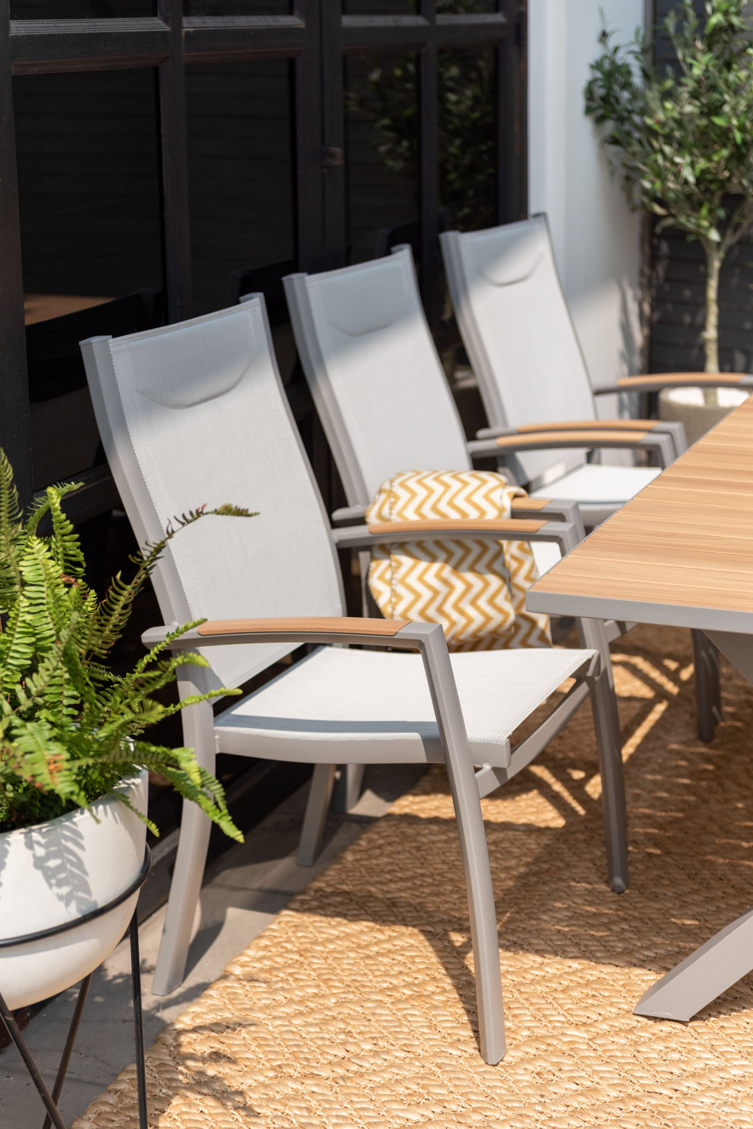 Outdoor dining chair with gray frame, white mesh back, and light wood armrests