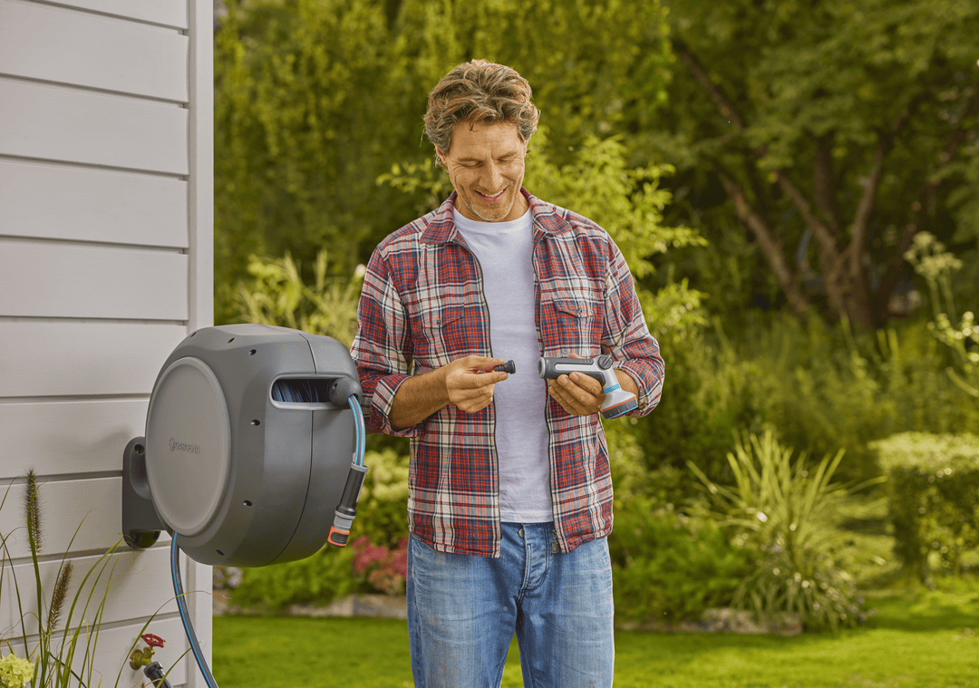 Retractable garden hose reel with gray housing, hose nozzle held outdoors