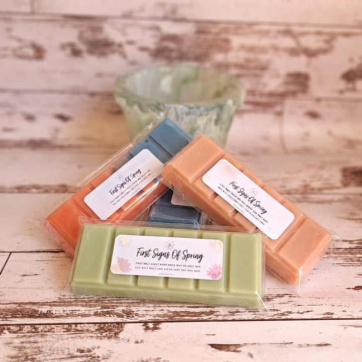Assorted wrapped wax melt bars in orange, green, and blue, shown in a clear tray