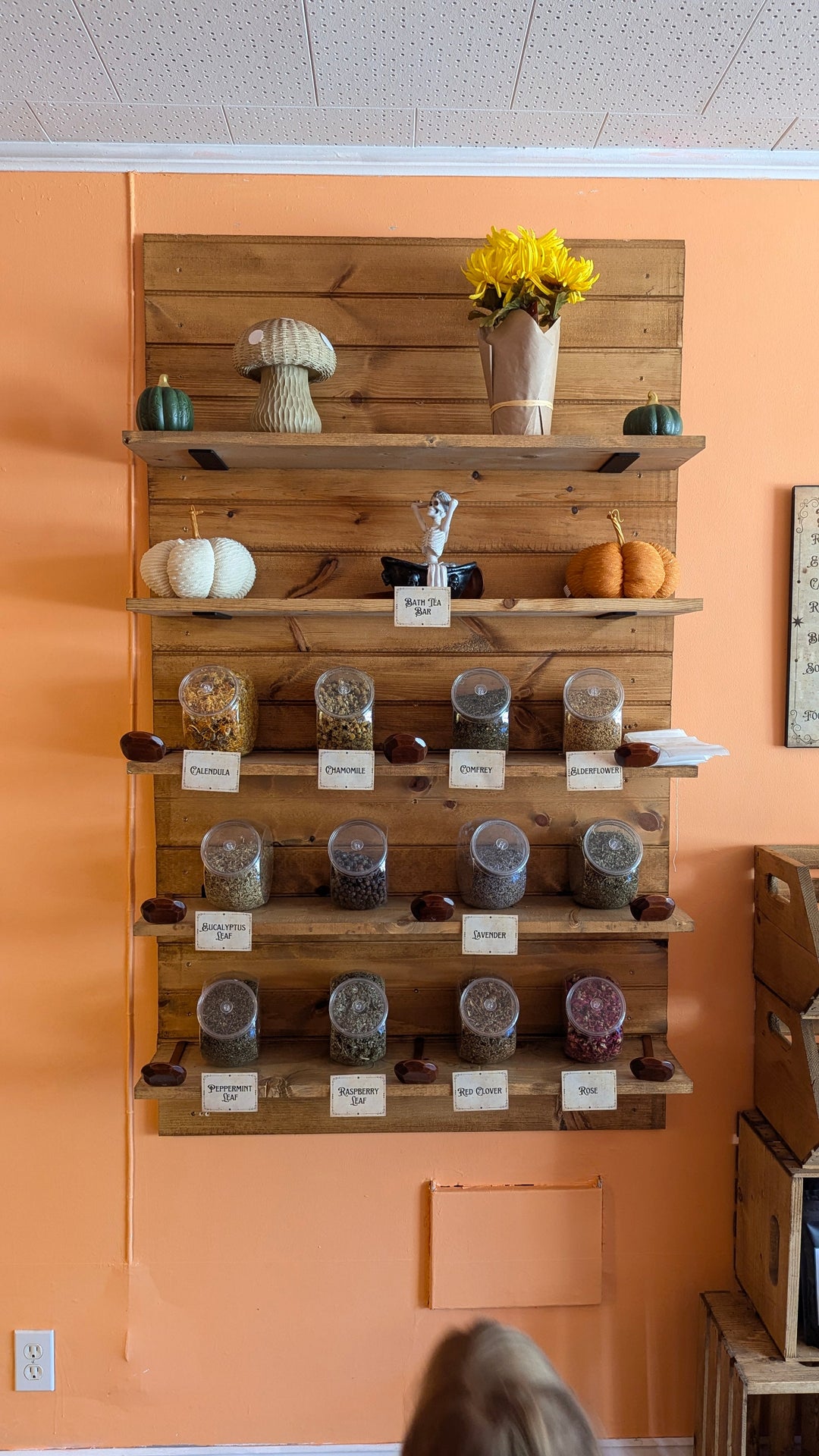 Wooden display shelf of labeled bath tea jars, with small bottles and scoops.