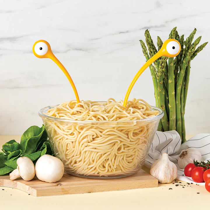 Yellow monster pasta servers holding noodles above a clear bowl