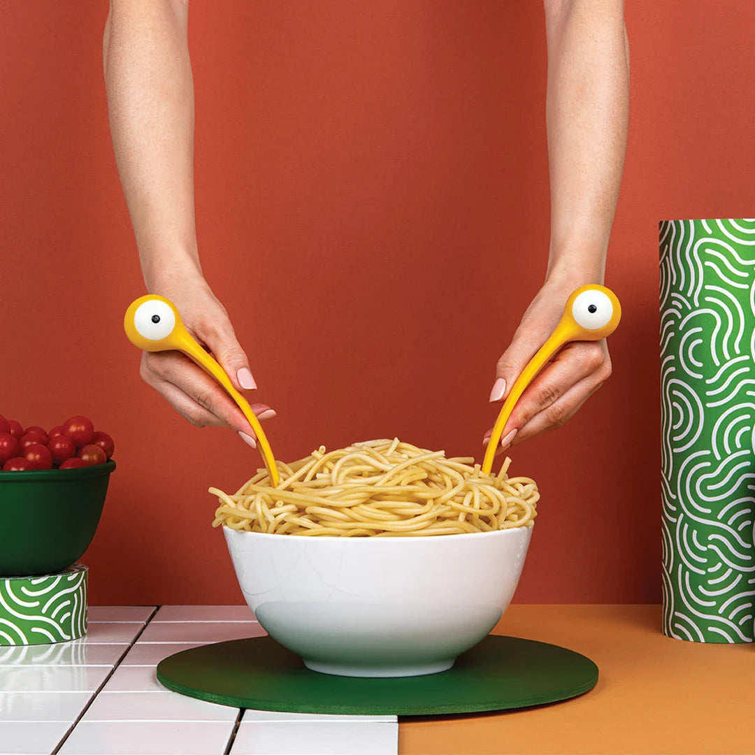 Yellow monster pasta servers in hands lifting spaghetti from a white bowl