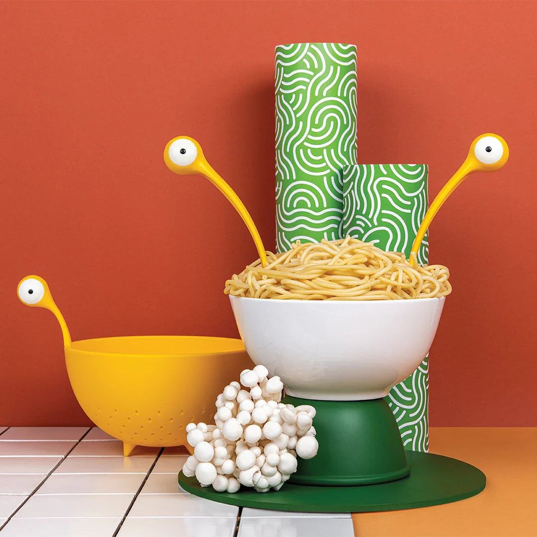 Yellow monster pasta server set standing in a white bowl of noodles