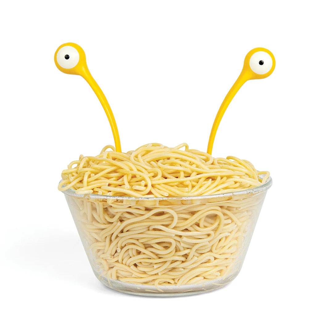 Clear bowl filled with spaghetti noodles held by two yellow monster-shaped servers