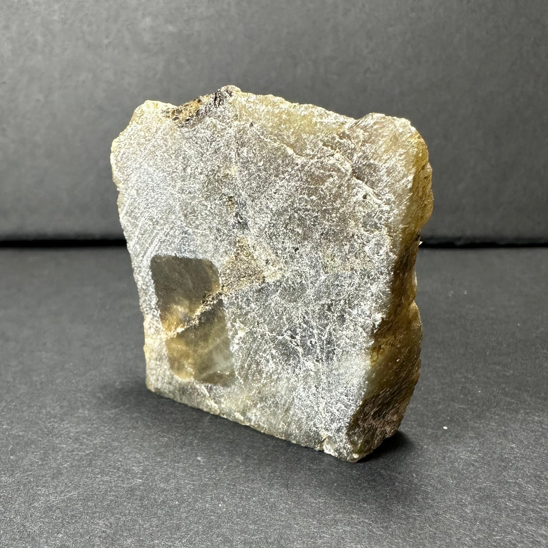 Labradorite rough stone with pale gray-white face and small dark pocket opening