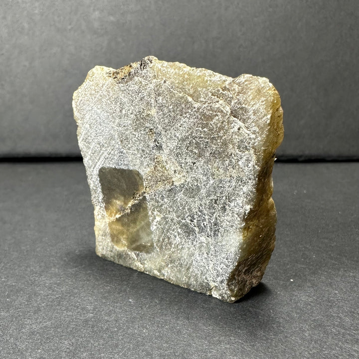Labradorite rough stone with pale gray-white face and small dark pocket opening