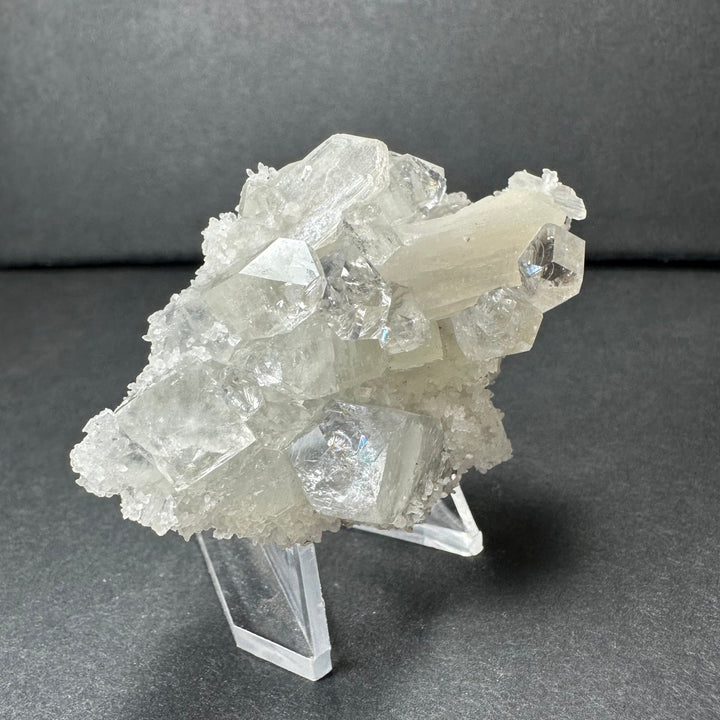 Clear apophyllite and white stilbite cluster with multi-faceted crystals, on stand