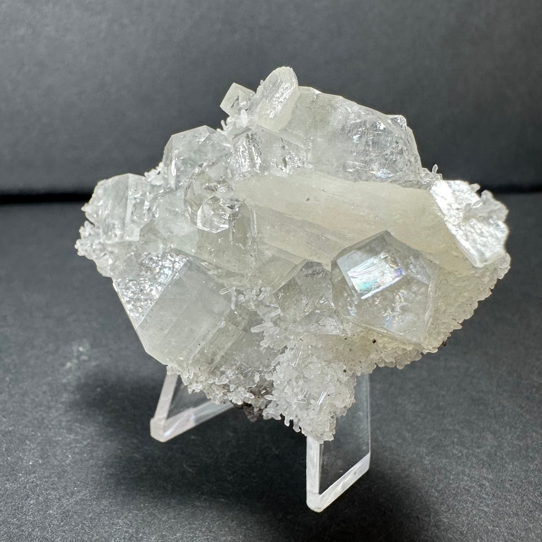 Clear apophyllite crystal cluster with white stilbite details, on clear tripod stand