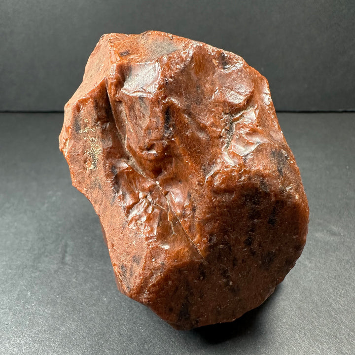 Raw reddish-brown obsidian stone, rugged surface with natural facets and irregular form
