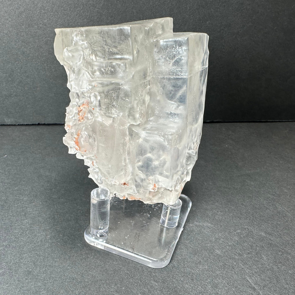 Colorless cubic fluorite mineral with orange speckle inclusions, angled on clear stand