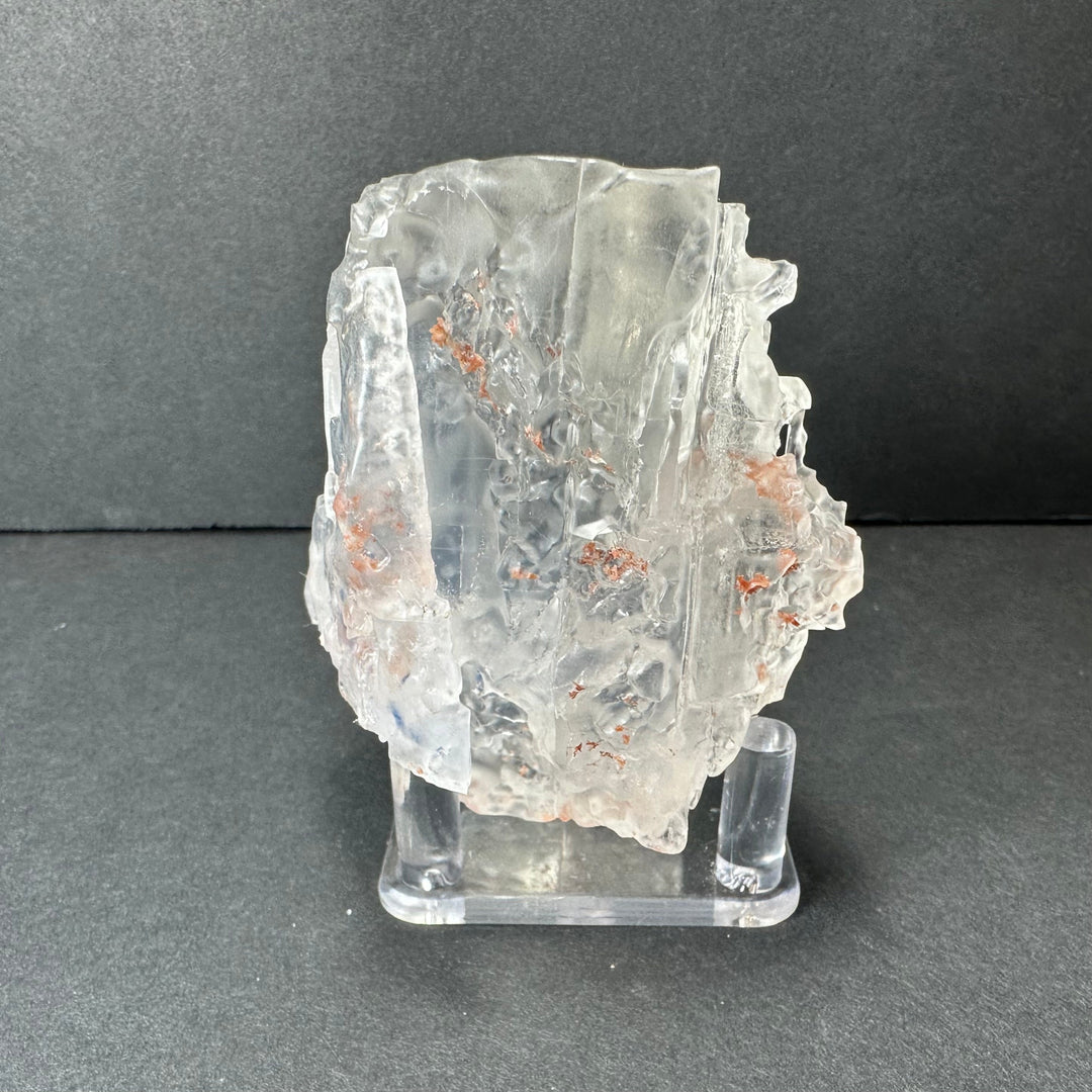 Colorless cubic fluorite mineral with orange speckled inclusions on clear display stand
