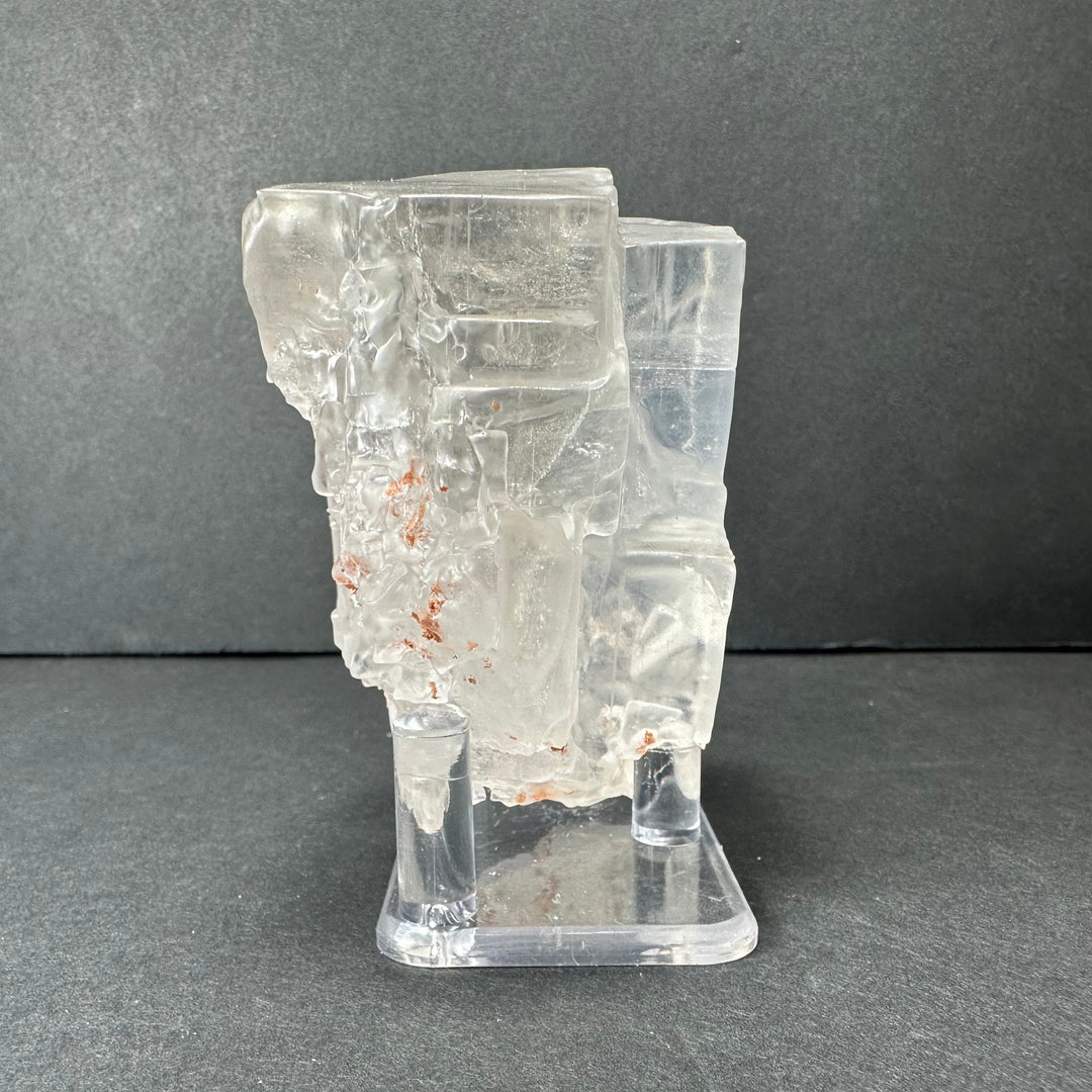 Colorless cubic fluorite mineral with orange speckle inclusions on clear display stand