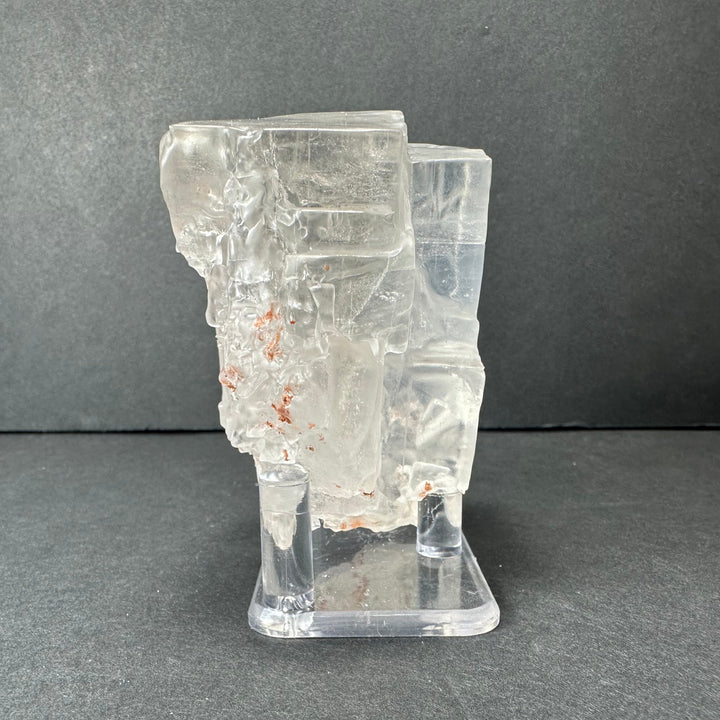 Colorless cubic fluorite mineral with orange speckle inclusions on clear display stand