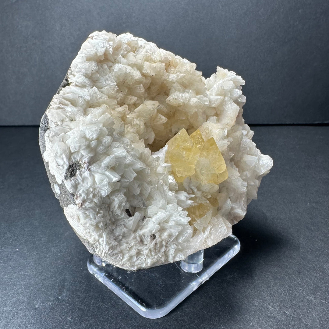 Yellow powellite and heulandite mineral specimen with white crystal matrix, on stand