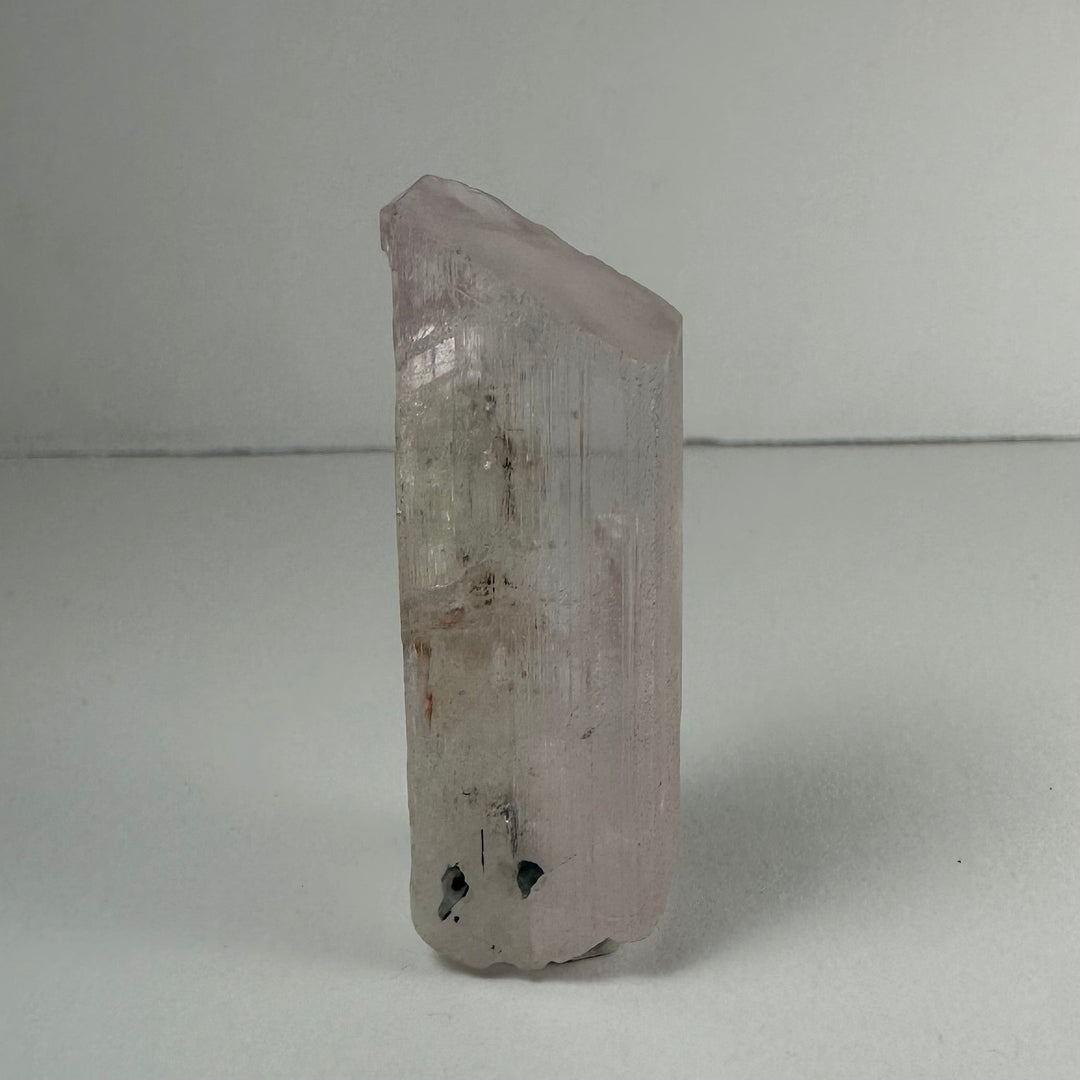 Terminated light pink kunzite crystal, faceted point with dark inclusions at base