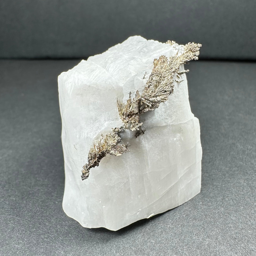 Calcite mineral specimen with silver-gray dendritic growth on white rock face
