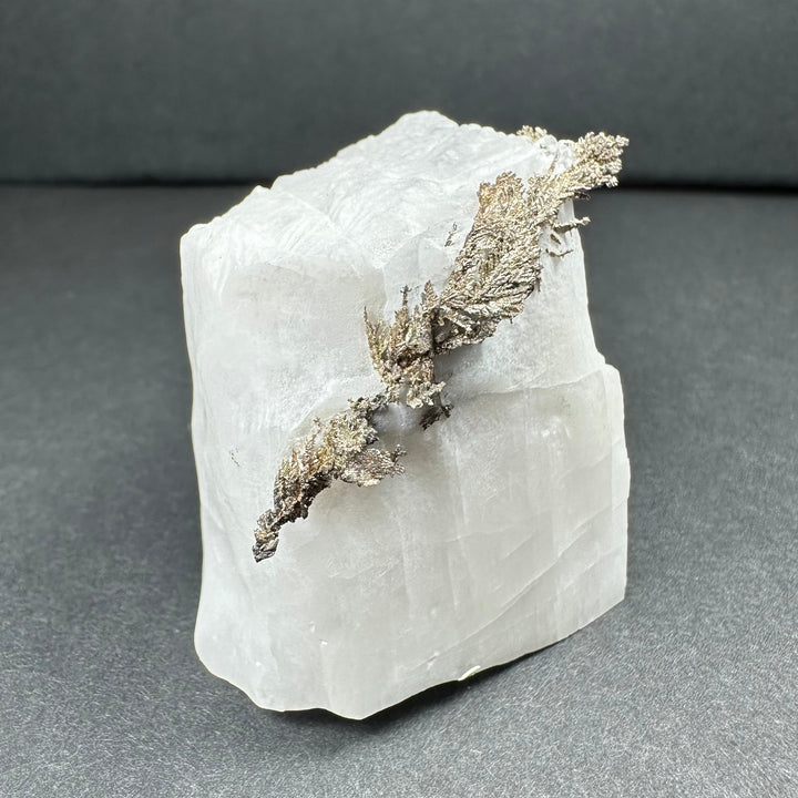 Calcite mineral specimen with silver-gray dendritic growth on white rock face