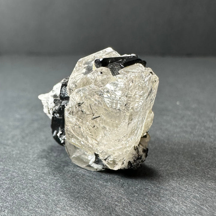 Mineral crystal specimen showing large clear quartz with black tourmaline and white inclusions.