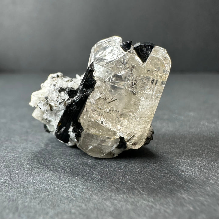Mineral crystal specimen featuring clear white quartz with black tourmaline on gray base.