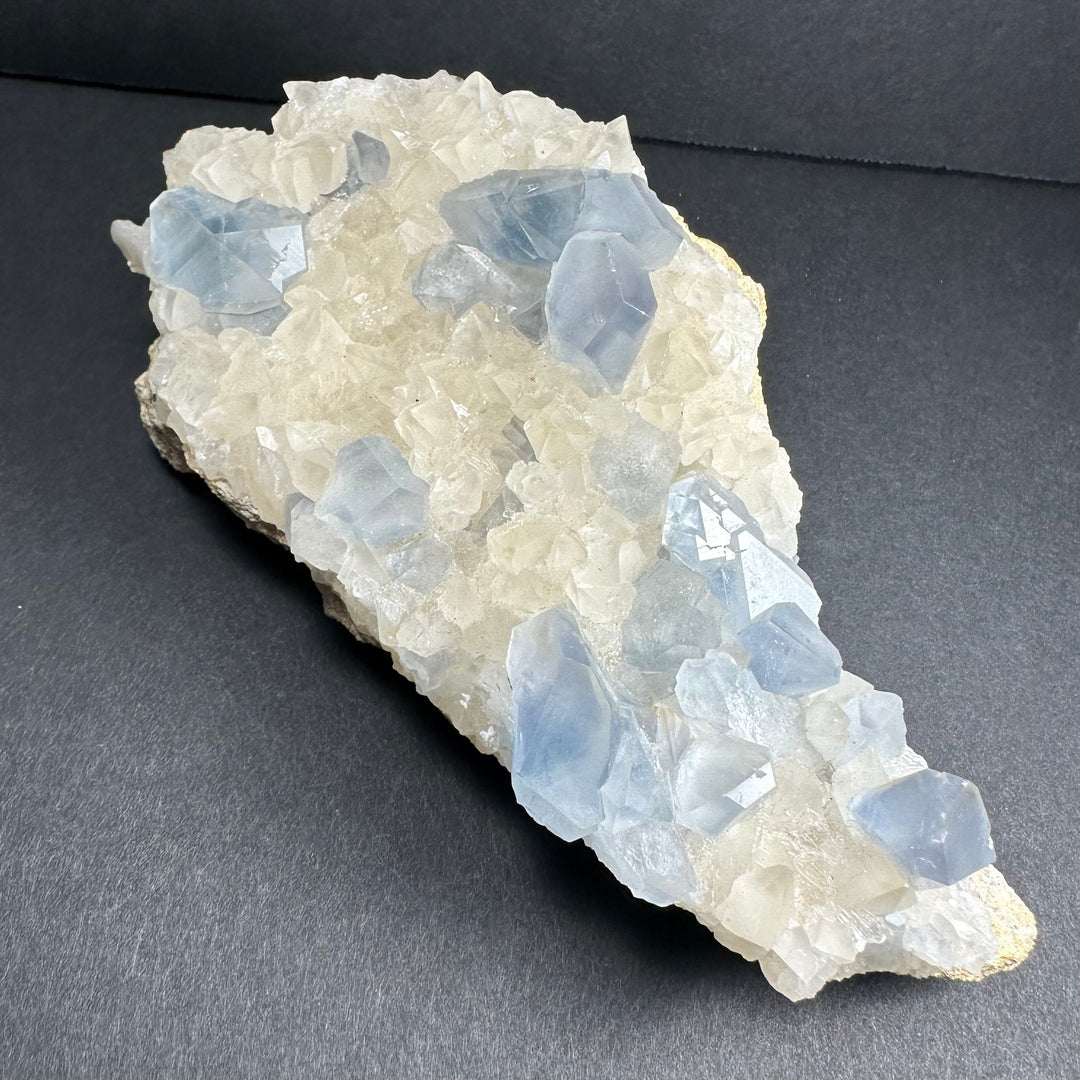 Oblong crystal cluster with light blue translucent points on a white matrix