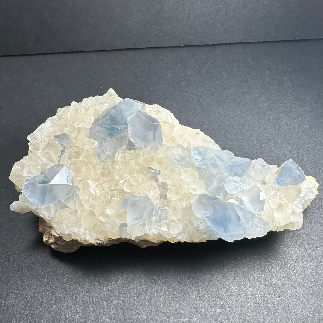 Celestite and calcite crystal cluster with blue translucent facets on white base