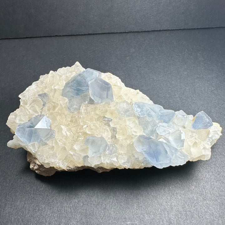 Celestite and calcite crystal cluster with blue translucent facets on white base