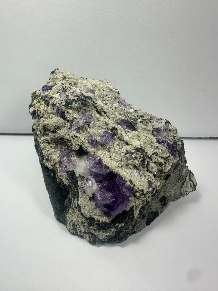 Purple fluorite crystal clusters on dark gray rock matrix specimen