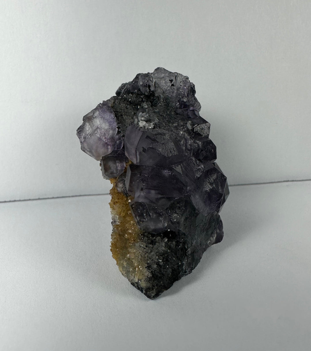 Purple fluorite crystal cluster on dark matrix rock with gold-tan streak