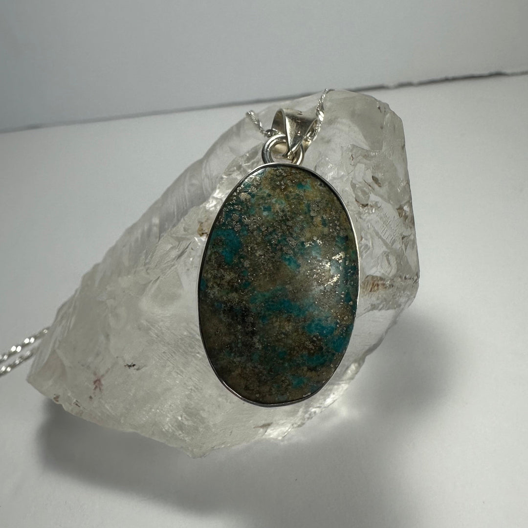 Oval turquoise stone pendant with silver-tone bail; blue-green mottled on chain.
