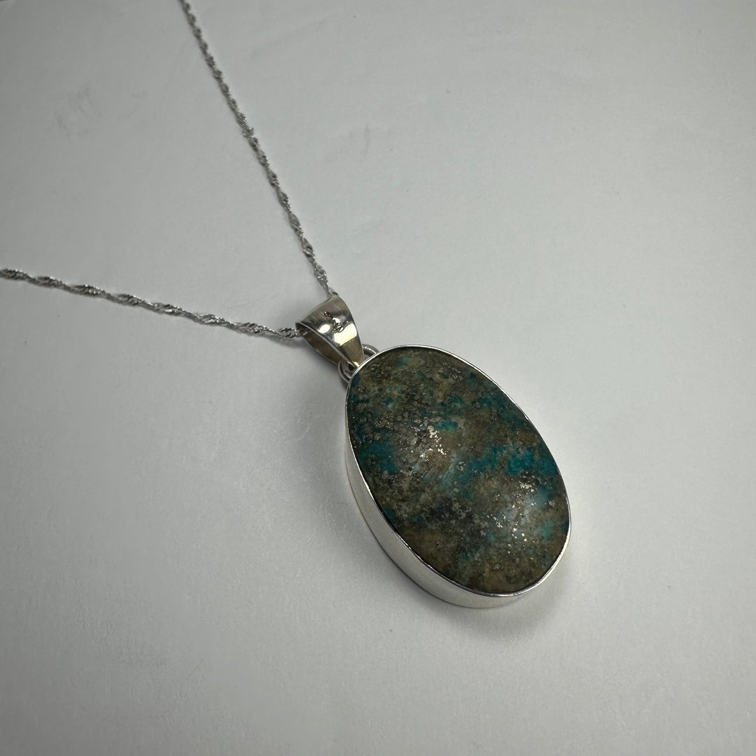 Oval turquoise stone pendant with silver-tone bail; dark blue-green speckled.