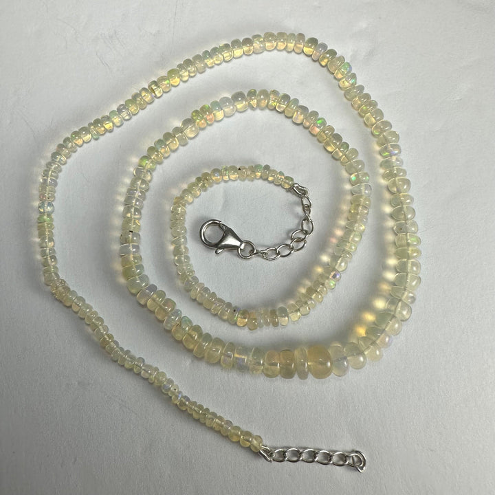 Triple strand opal-like bead necklace with silver clasp and adjustable chain, laid flat