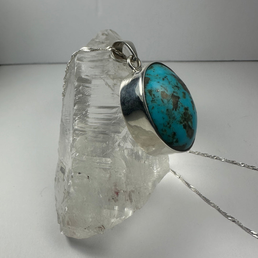 Oval turquoise stone pendant with silver frame and bail, side view on chain
