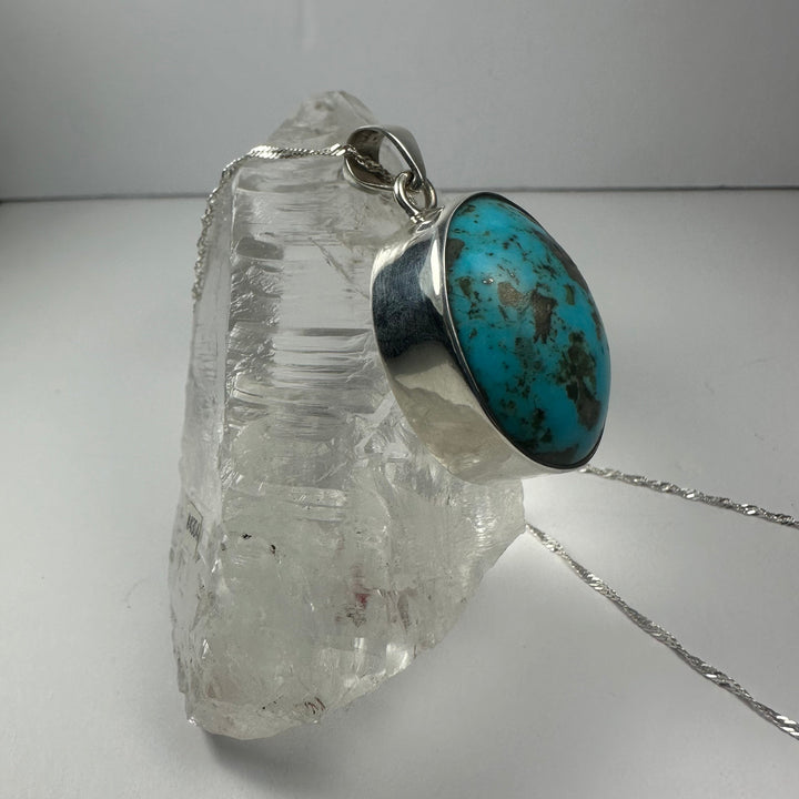 Oval turquoise stone pendant with silver frame and bail, side view on chain
