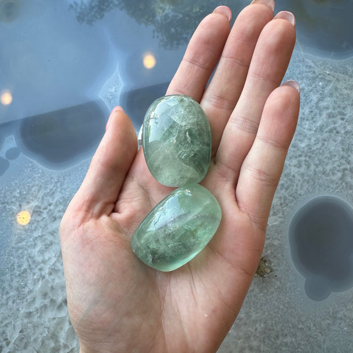 Two translucent green tumbled fluorite stones held in a palm