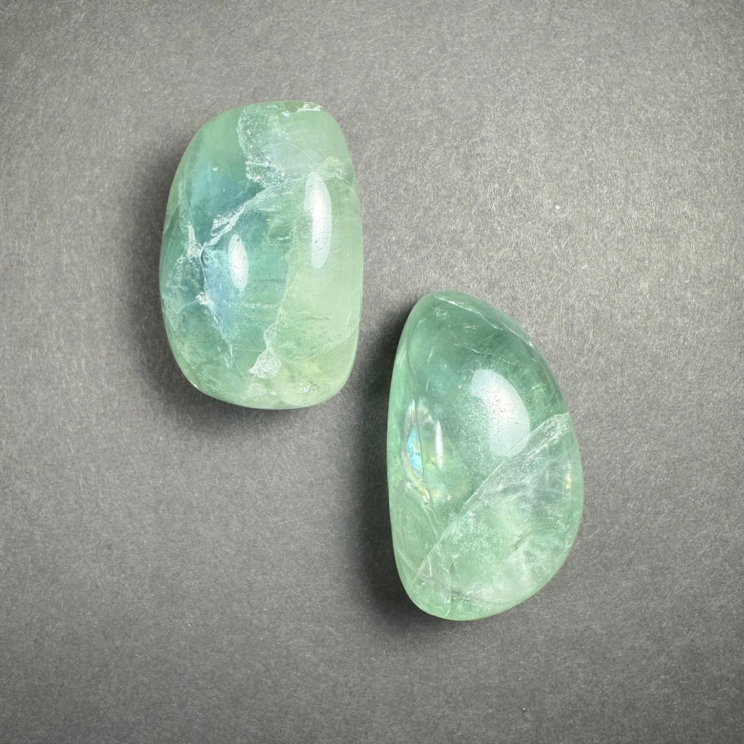 Pair of translucent green tumbled fluorite stones on a gray surface