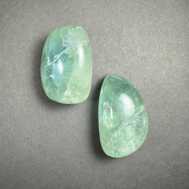 Pair of translucent green tumbled fluorite stones on a gray surface