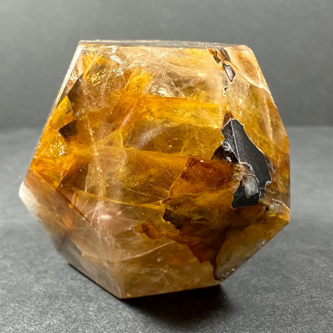 Yellow hematoid quartz dodecahedron with bright facets and scattered dark stone inclusions