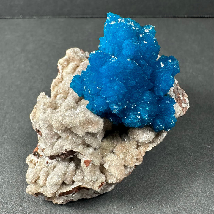 Bright blue cavansite cluster on gray-beige stilbite and stone matrix, angled view