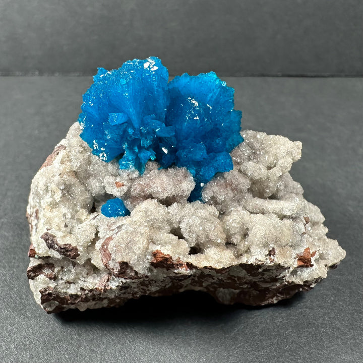 Vivid blue cavansite crystals over pale white stilbite on rough rock base